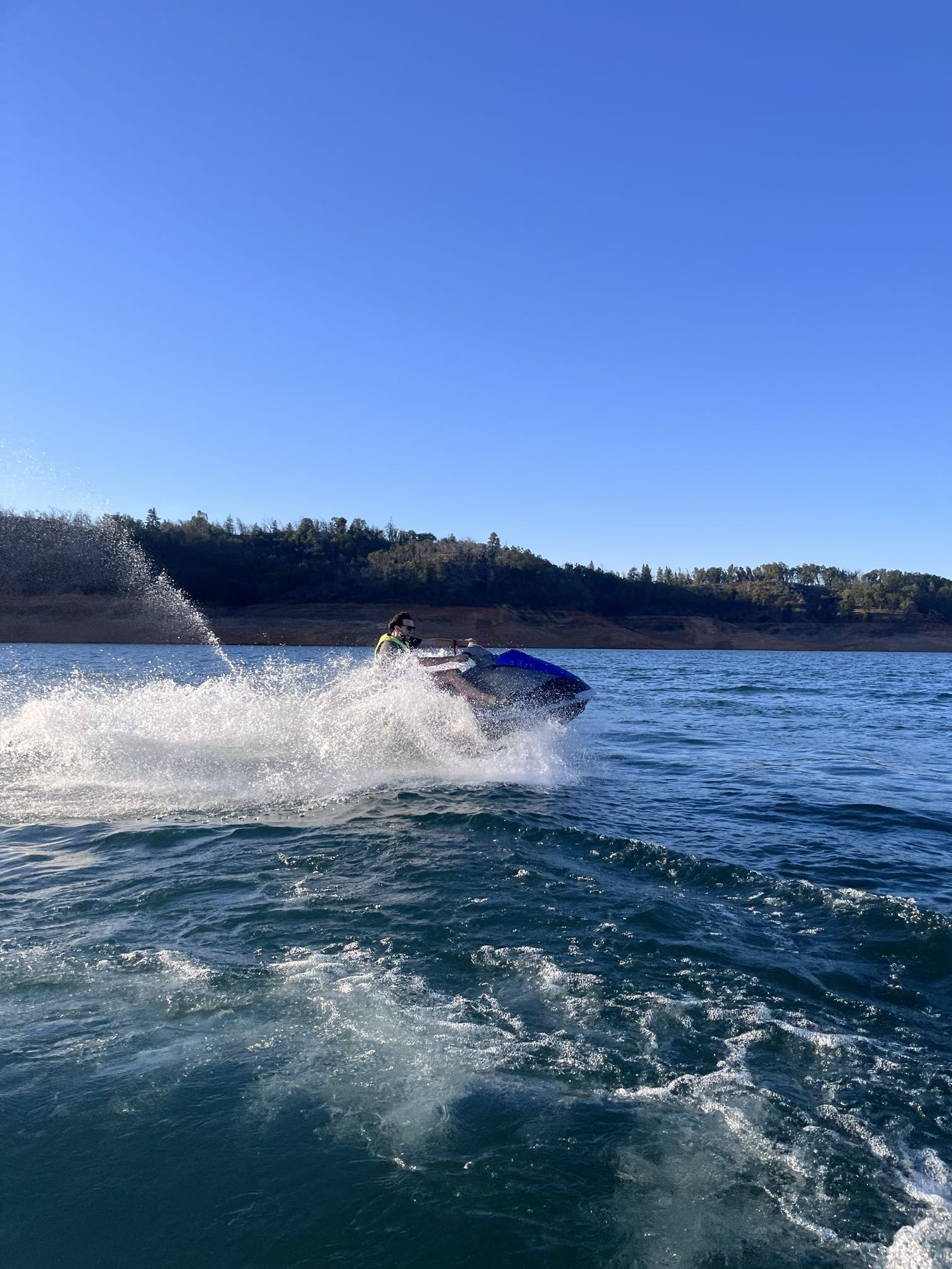 A rider carving the blue WaveRunner hard and kicking up a big wall of white spray against deep blue water and sky