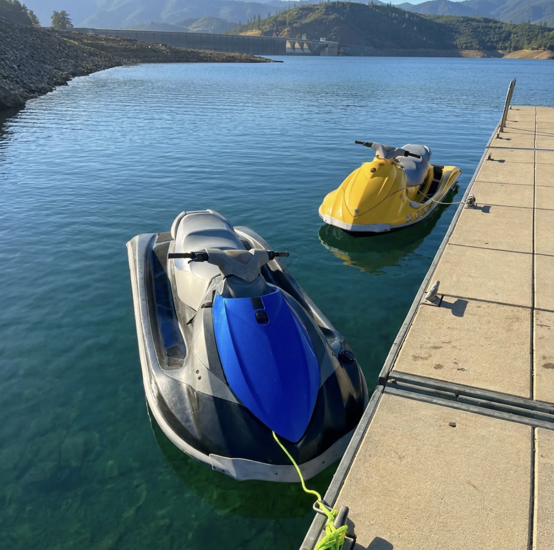 High-angle view of the blue and yellow WaveRunners moored at the dock in clear teal water with the dam in the distance