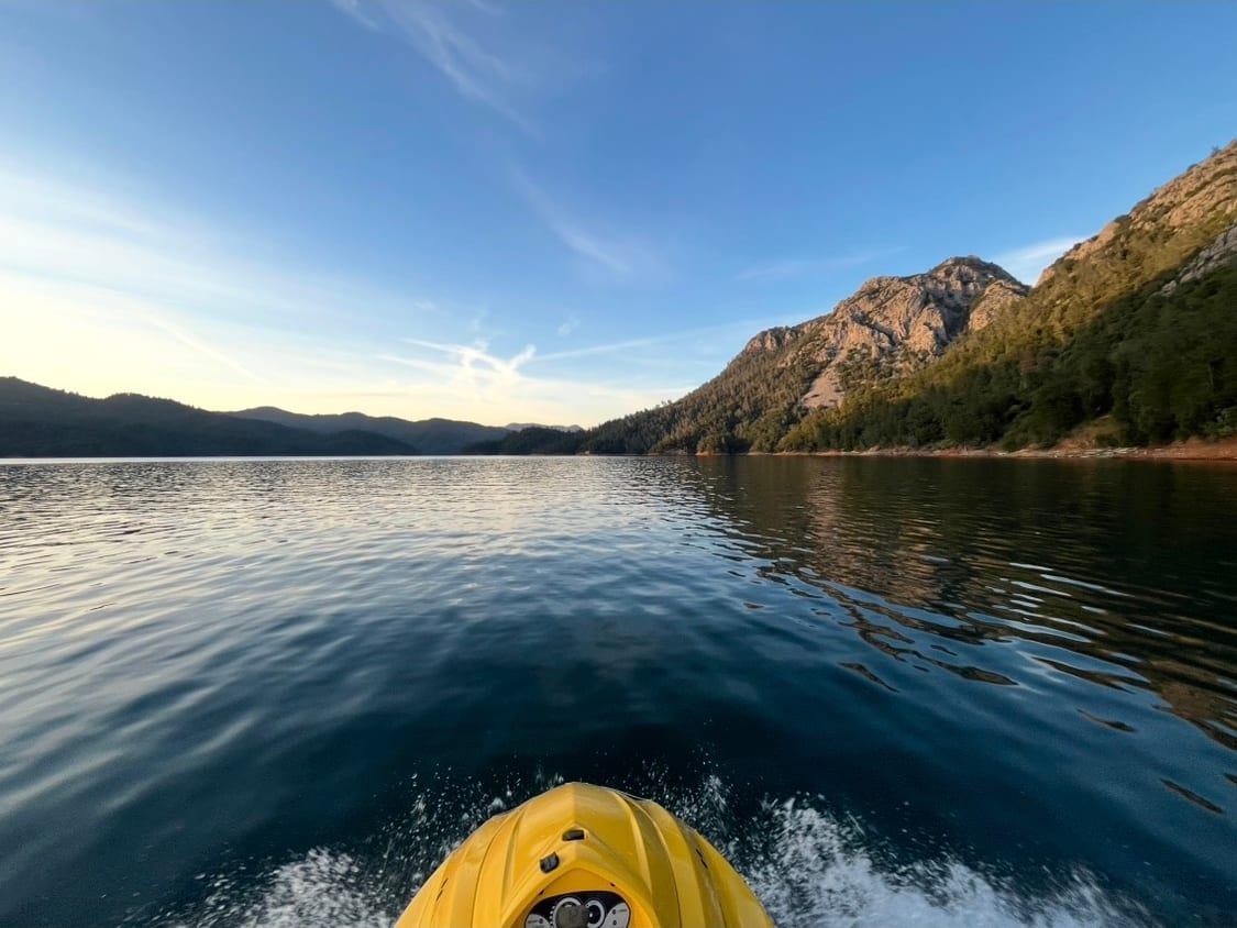 Point of view from a jet ski cruising toward a granite peak across mirror-flat water at dusk