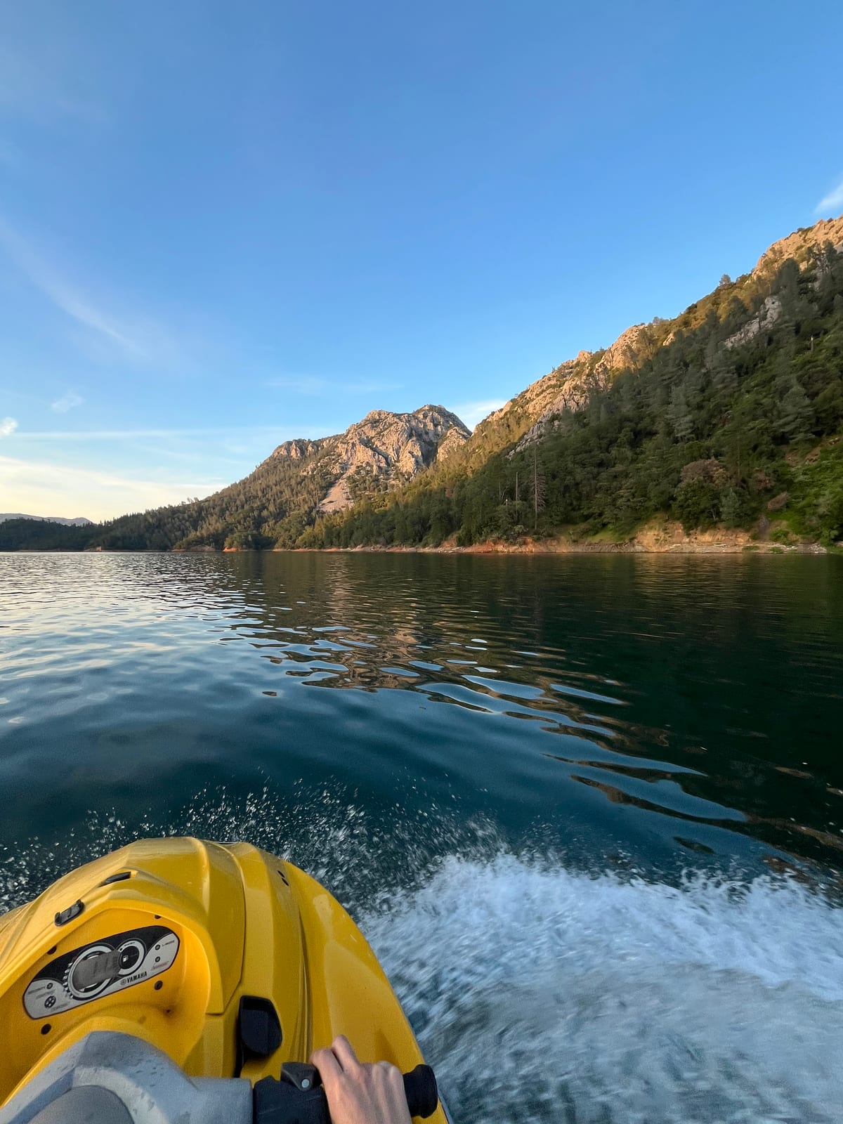 Point of view alongside a sunlit granite and pine ridge with the jet ski wake curling away