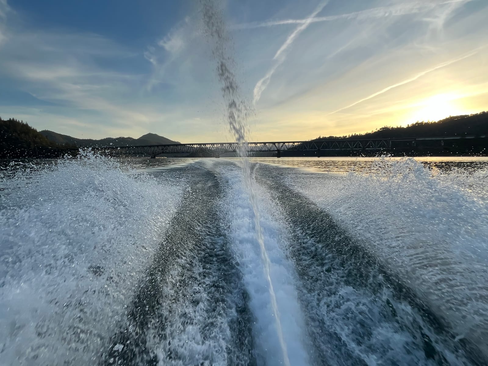 Looking back at the twin rooster tail wake of a jet ski with the Pit River Bridge silhouetted against a sunset